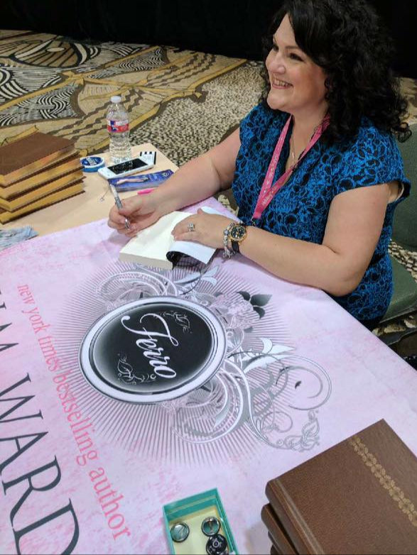 H.M. Ward sitting at a table at a book event signing a book.